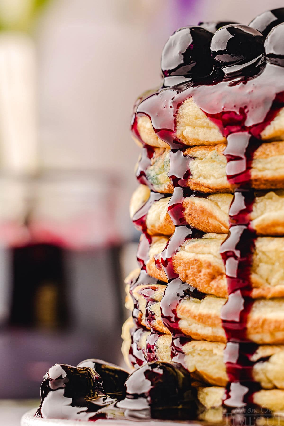 super close up look at blueberry sauce being drizzled off the side of a stack of pancakes.