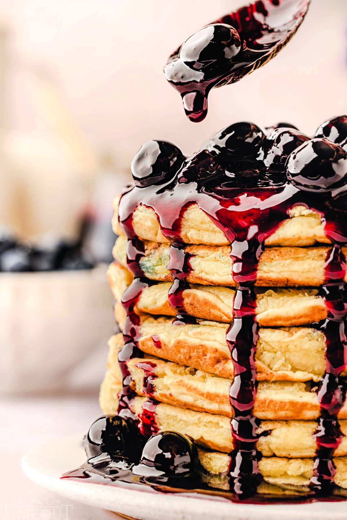 Blueberry sauce being drizzled over the top of a seriously impressive stack of lemon ricotta pancakes.