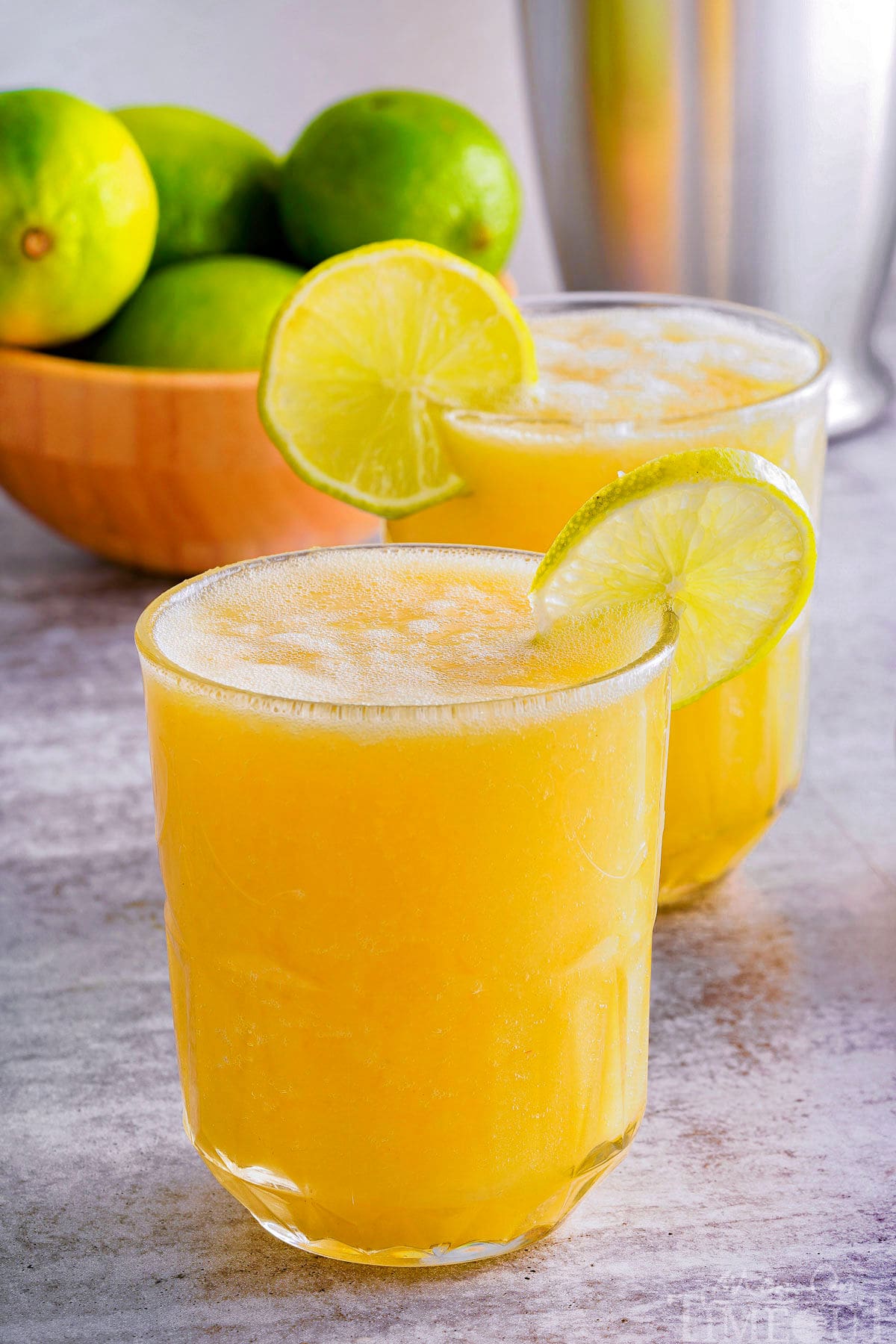 side view of two glasses of pineapple mango mocktail in a glass with a lime wedge garnish on the rim