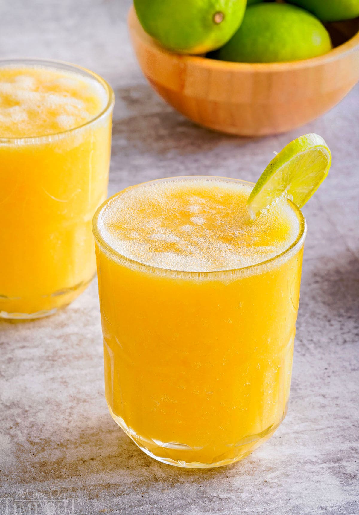 side view of a pineapple mango mocktail in a glass with a lime wedge garnish on the rim.