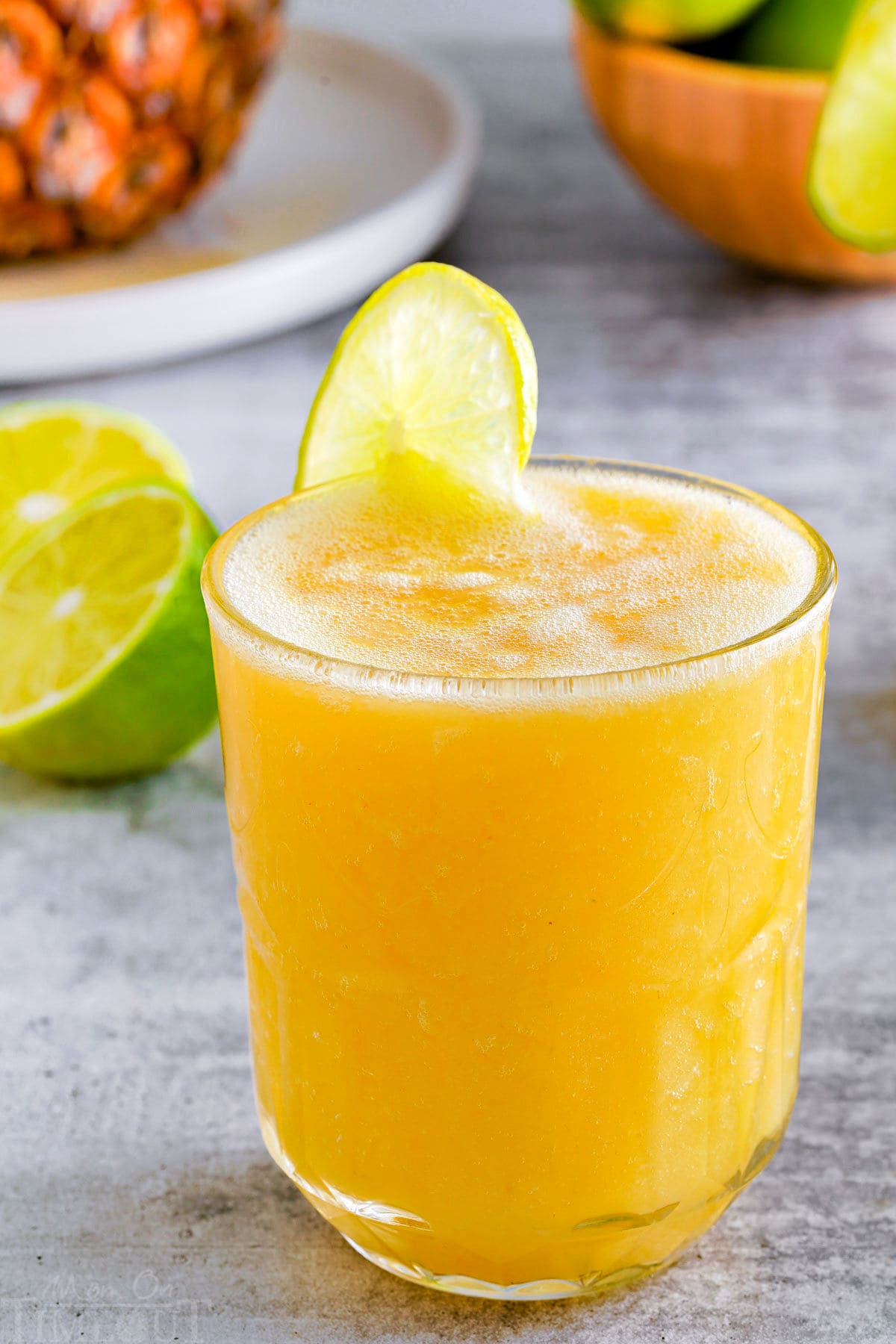 side view of a pineapple mango mocktail in a glass with a lime wedge garnish on the rim.