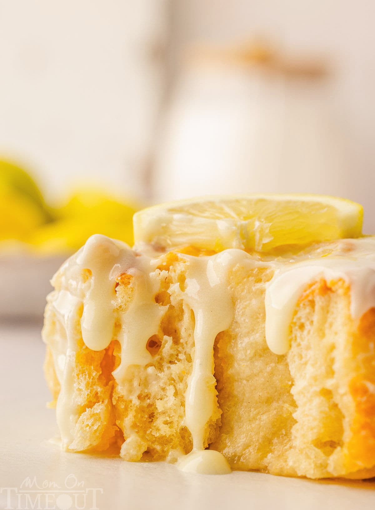 A side view of a lemon roll with glaze dripping down and a bite taken out of it.