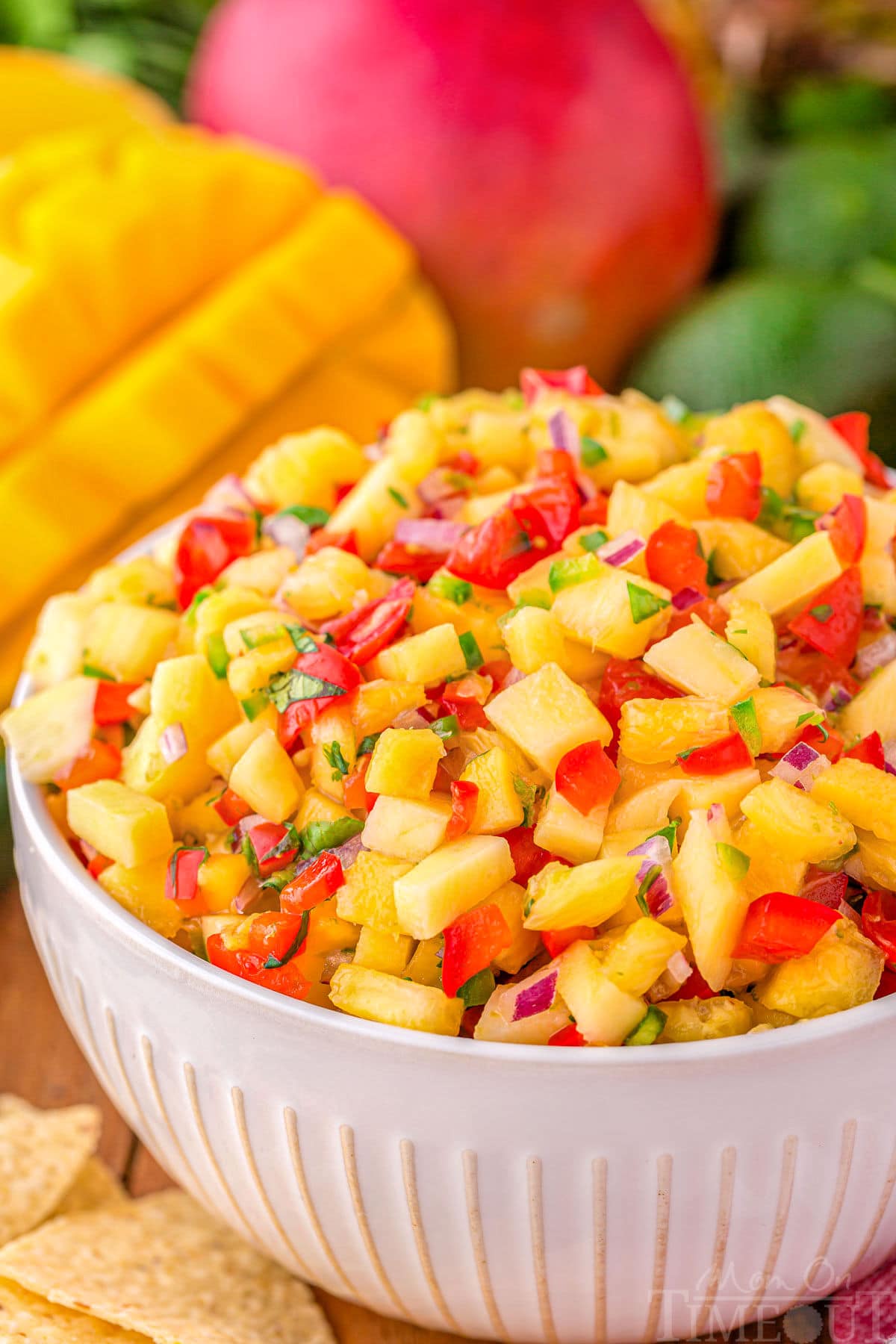 serving bowl filled withe pineapple mango salsa ready to be enjoyed. Mangoes can be seen in the background.