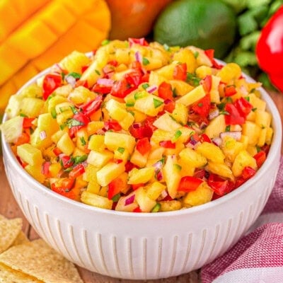 serving bowl filled withe pineapple mango salsa ready to be enjoyed. Mangoes can be seen in the background.