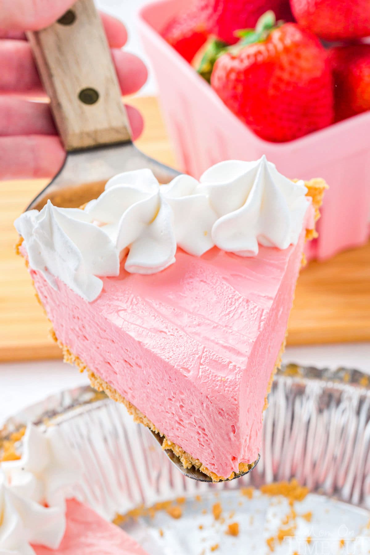 Piece of kool aid pie topped with whipped cream being held up over the rest of the pie.