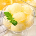 A glass bowl with lots of scoops of lemon sorbet with a mint leaf garnishing it.