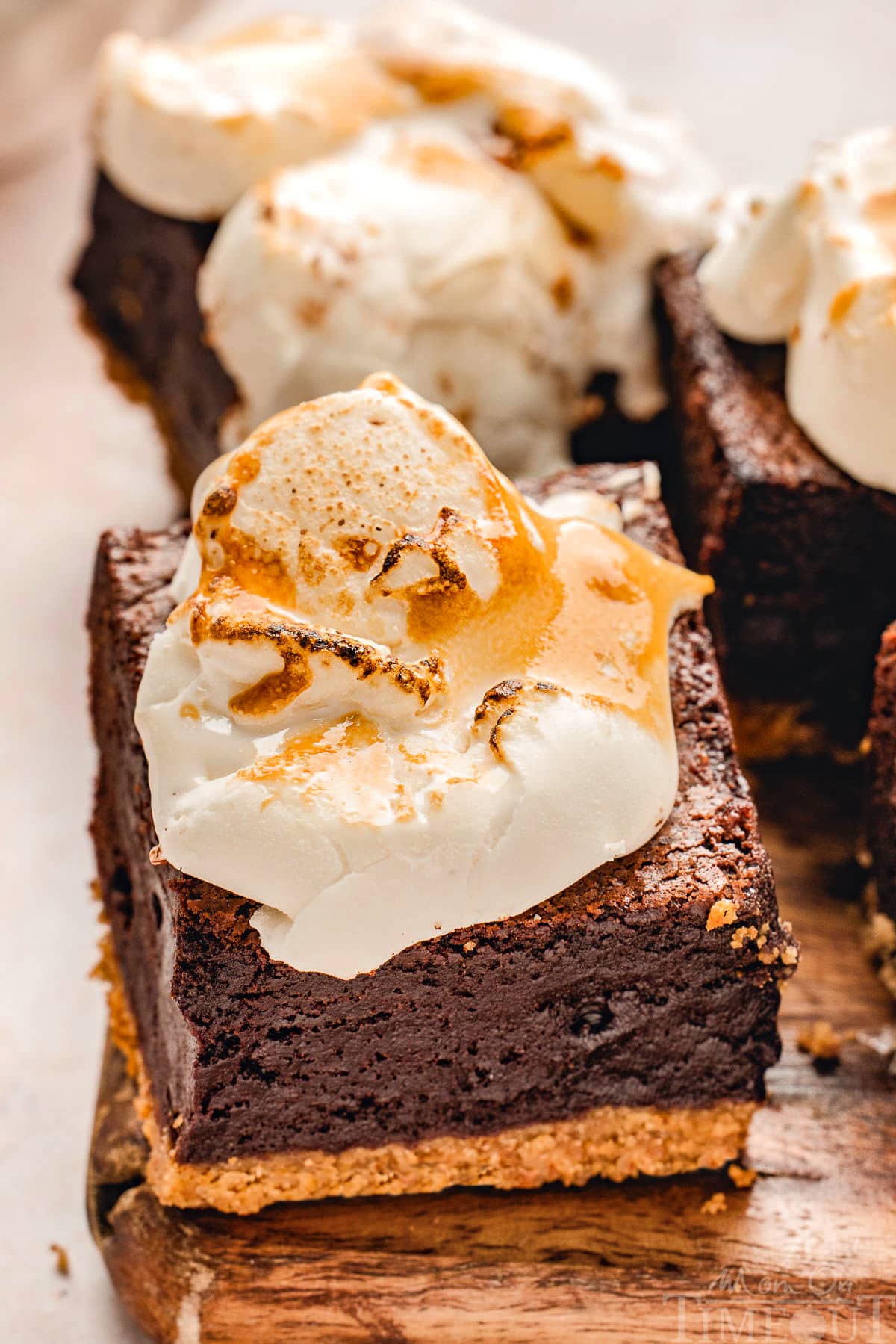 Smores brownies made with graham cracker crust and topped with torched marshmallow sitting on wood board.