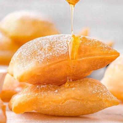 A stack of sopapillas with a honey dipper drizzling honey on top.