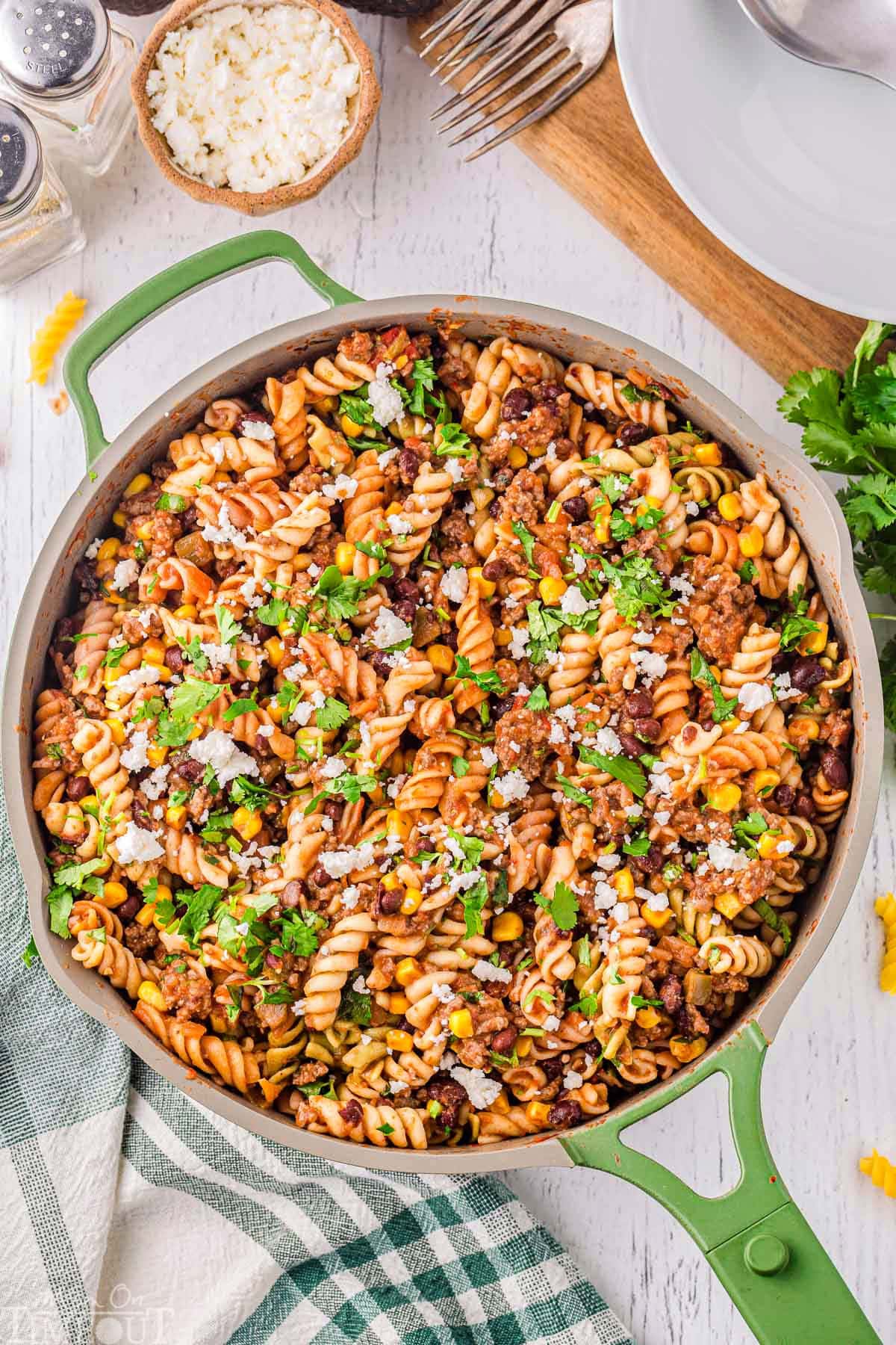 Top down view of green skillet filled with taco pasta recipe garnished with cilantro and queso fresco.