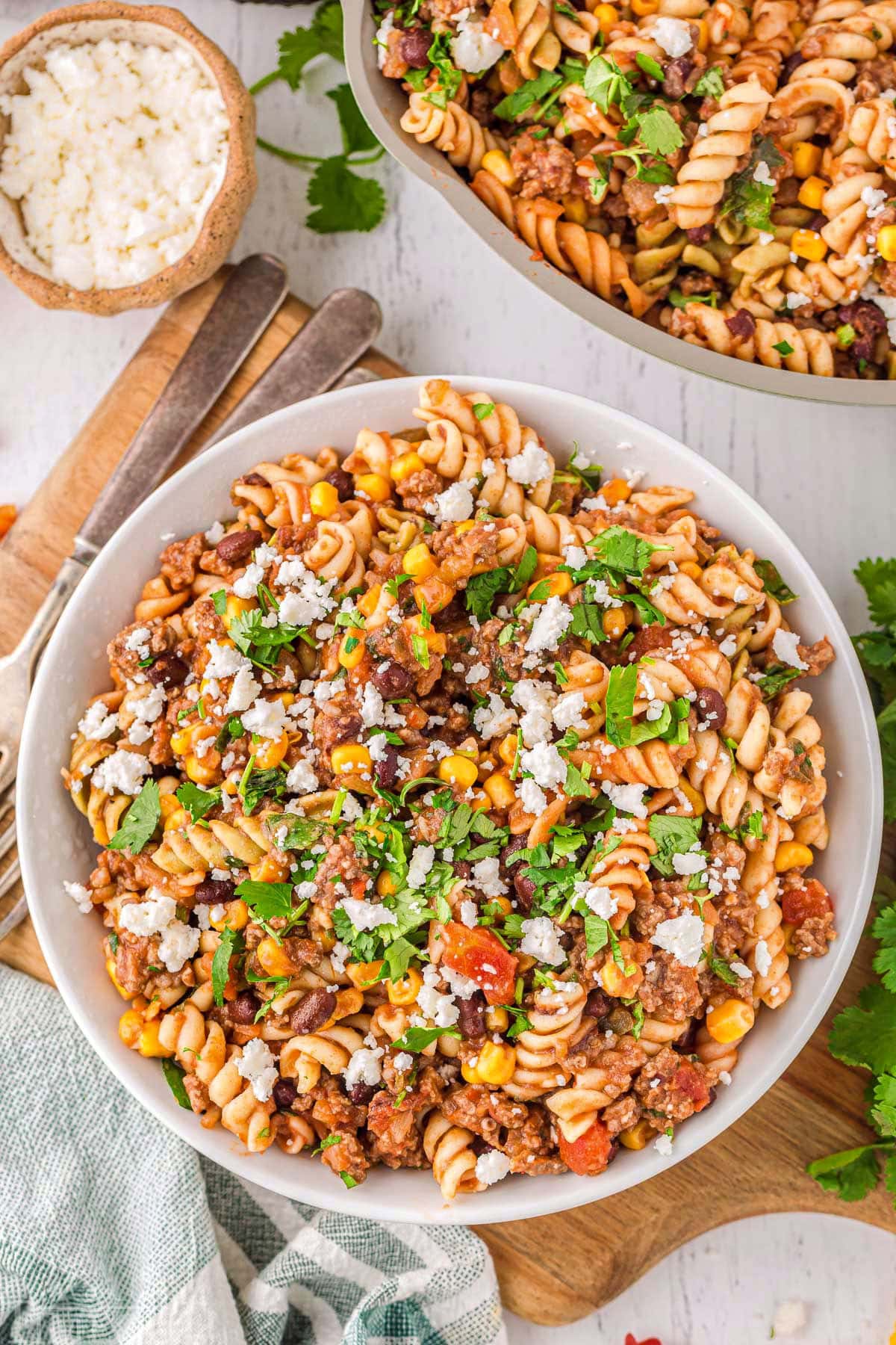Top down view of taco pasta in a round white bowl next to the skillet with the rest of the pasta.