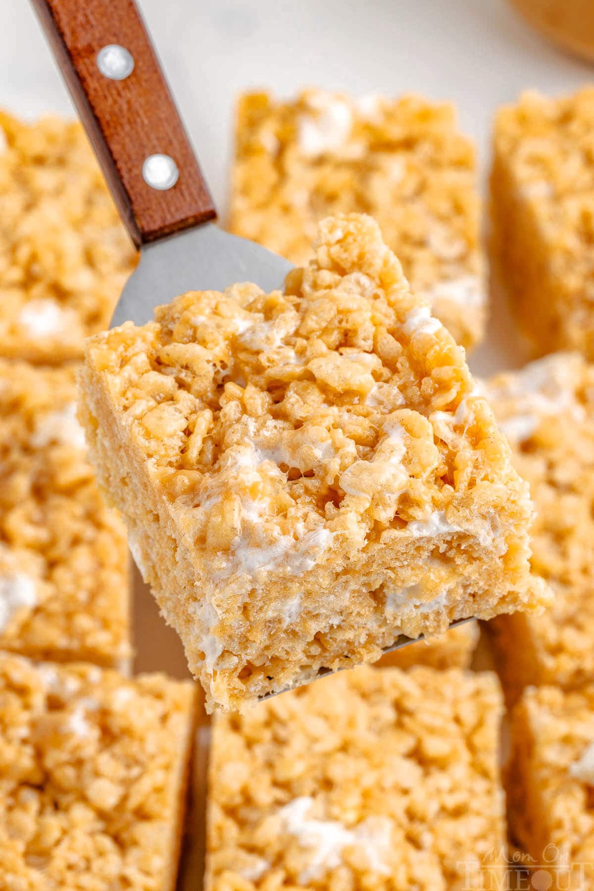 Metal server holding up peanut butter rice krispie treat over the rest of the cut treats.