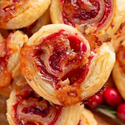 Top down shot of brie and cranberry puff pastry pinwheels stacked on a wood board.
