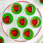 A top down view of grinch jello shots on a white plate with a red rim.