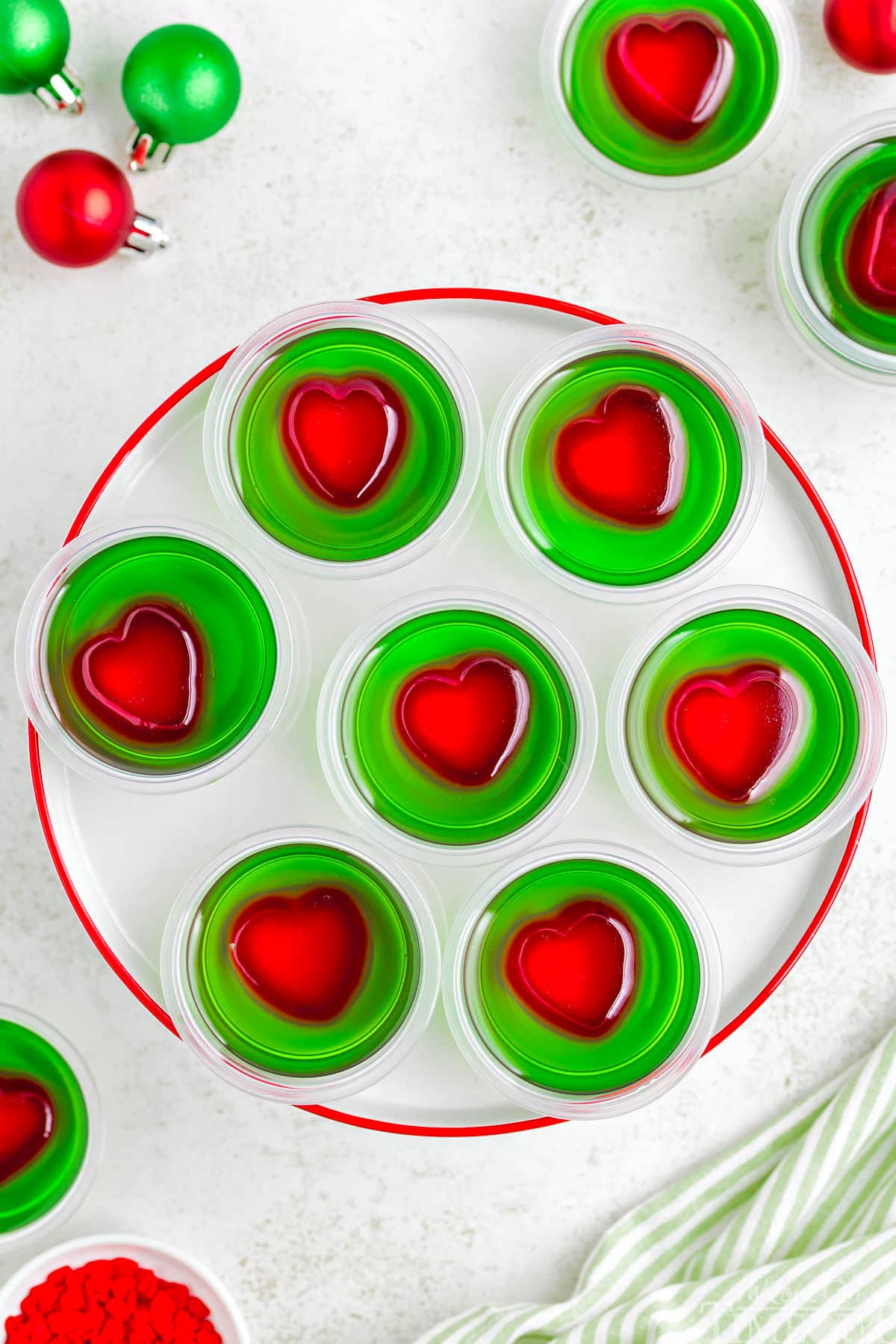 A top down view of grinch jello shots on a white plate with a red rim.