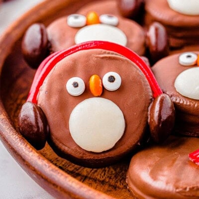 OREO Penguin propped up on a wood tray next to more penguin cookies. Penguin has red earmuffs.