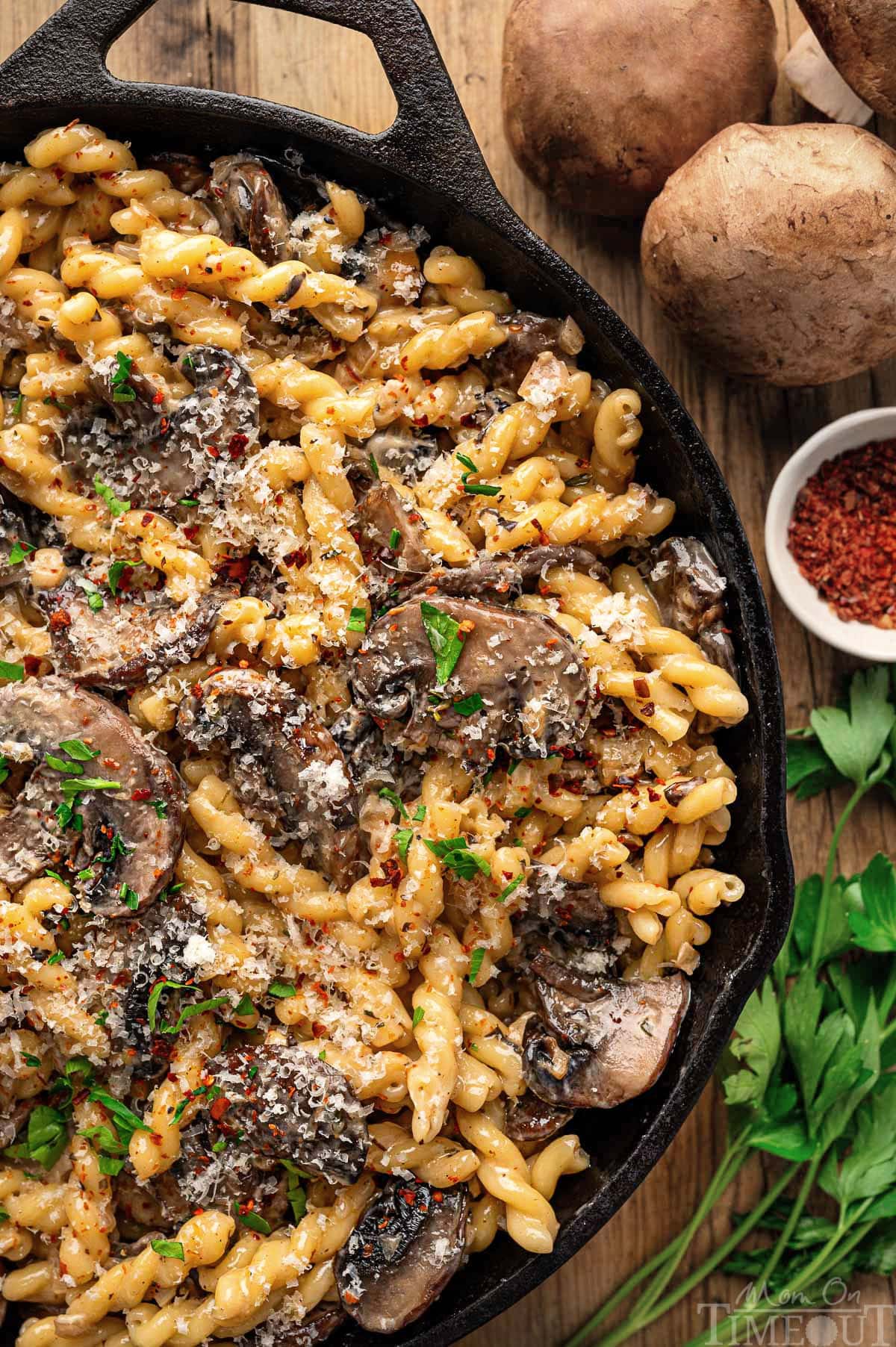 Close up look at mushroom pasta sauce recipe in a cast iron skillet sitting next to mushrooms and herbs.