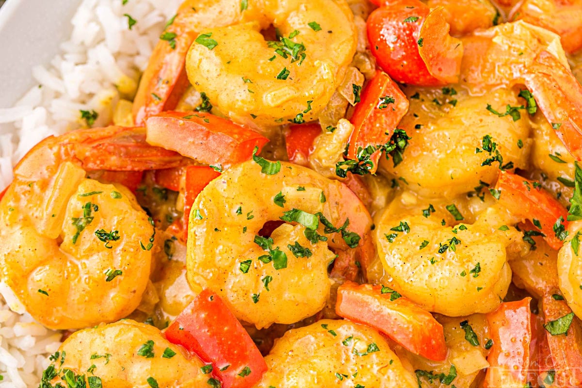 Pieces of shrimp and red bell pepper in creamy coconut curry sauce. The curry is on a bed of white rice.