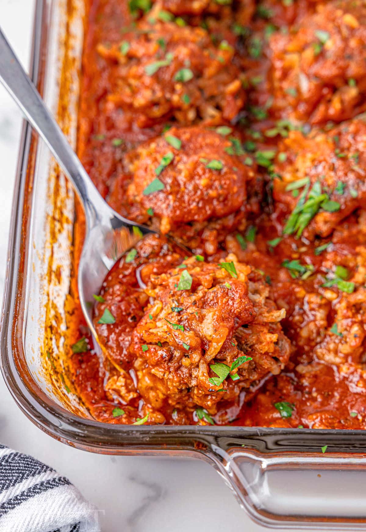 Porcupine meatballs in a glass baking dish. A metal spoon is holding one of the meatballs.