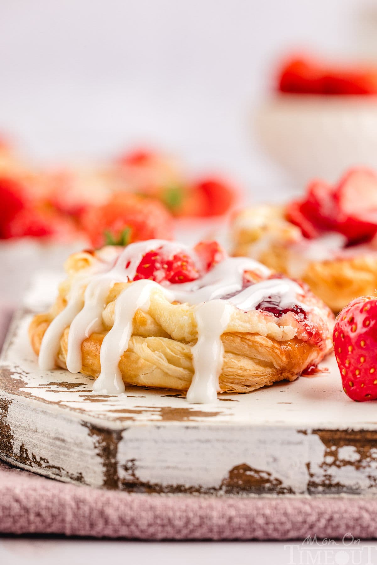 Strawberry cream cheese danish with glaze drizzled on top sitting on white wood board.