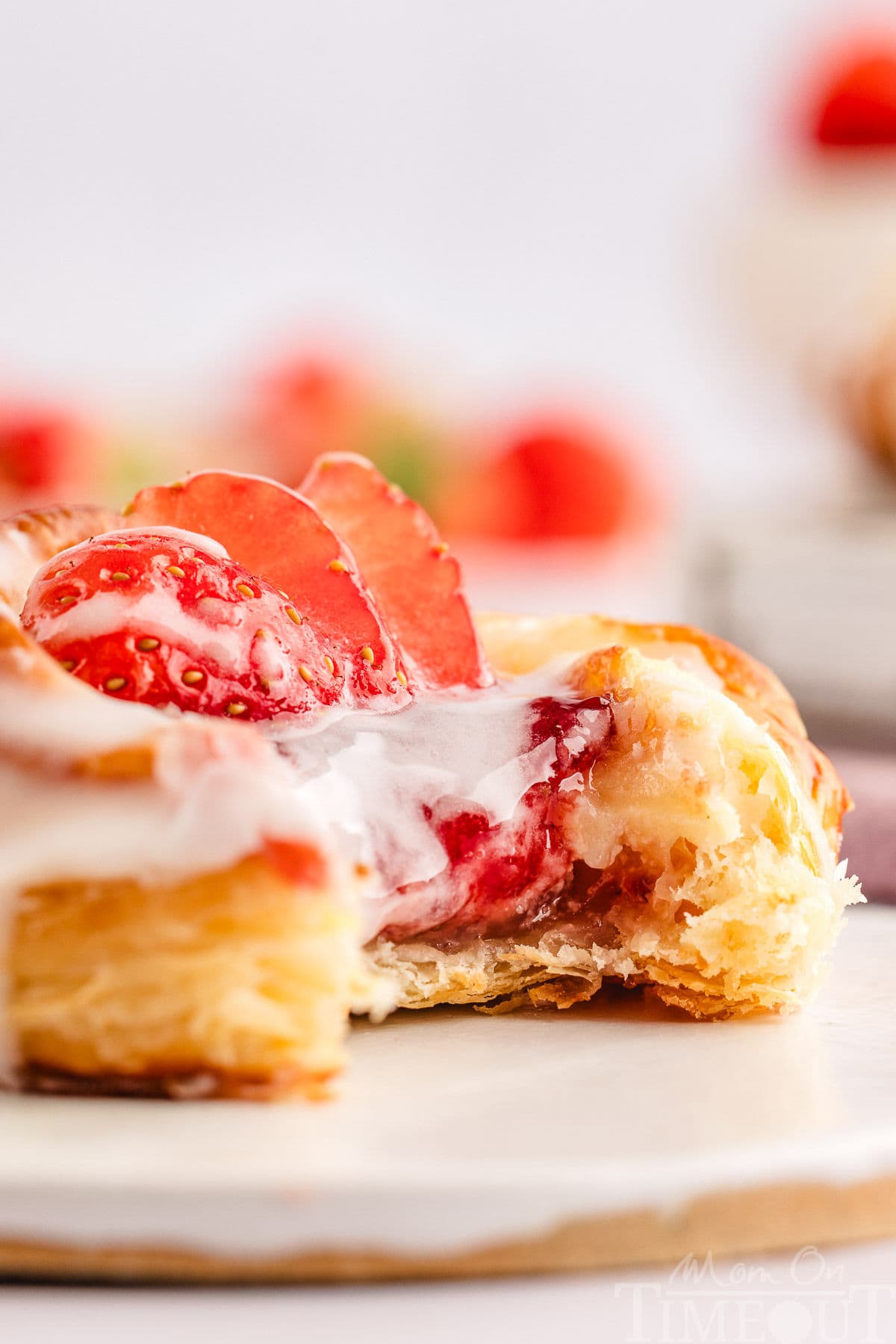 Strawberry cream cheese danish with glaze drizzled on top sitting on white wood board with bite taken.