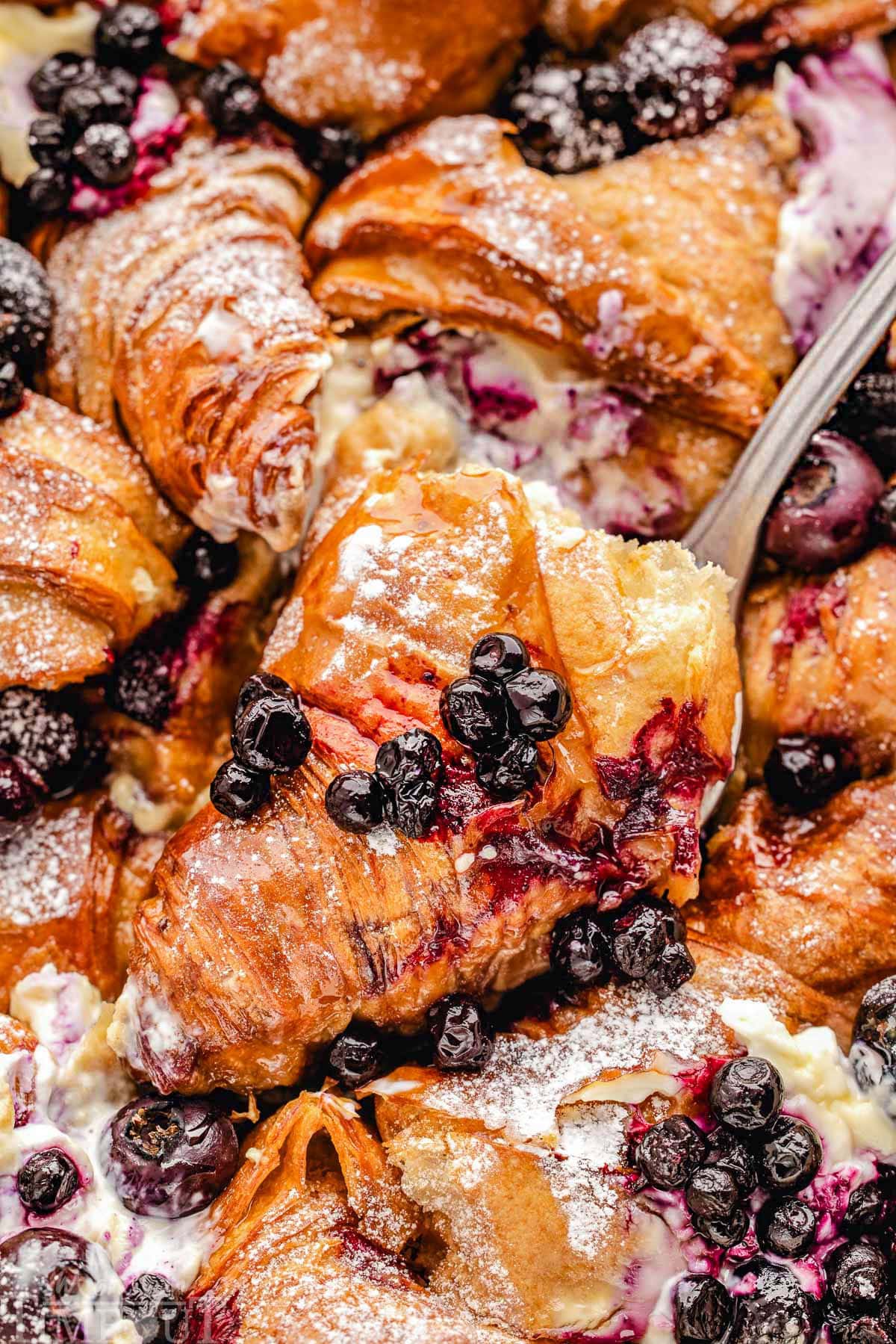 Piece of blueberry croissant french toast bake being lifted out of the casserole dish.