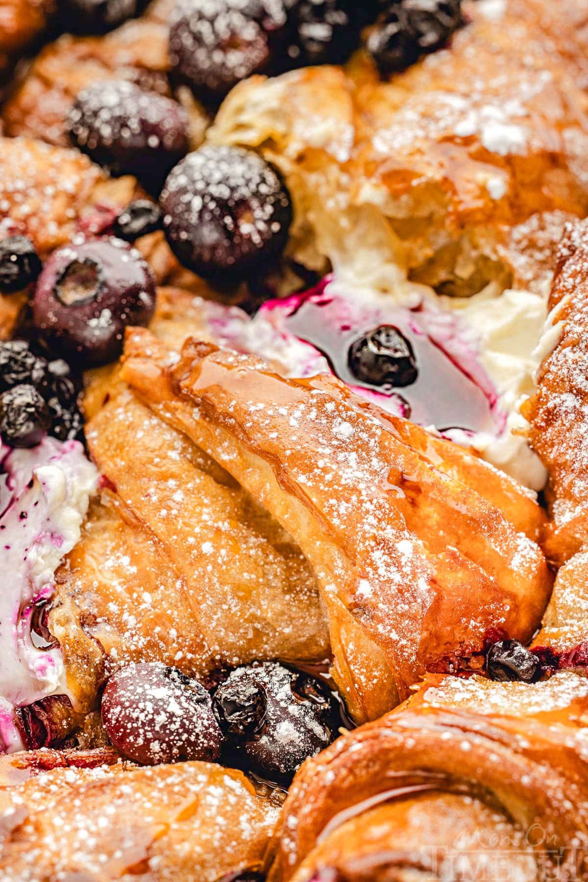 Close up look at maple syrup glistening on croissant french toast bake with blueberries.