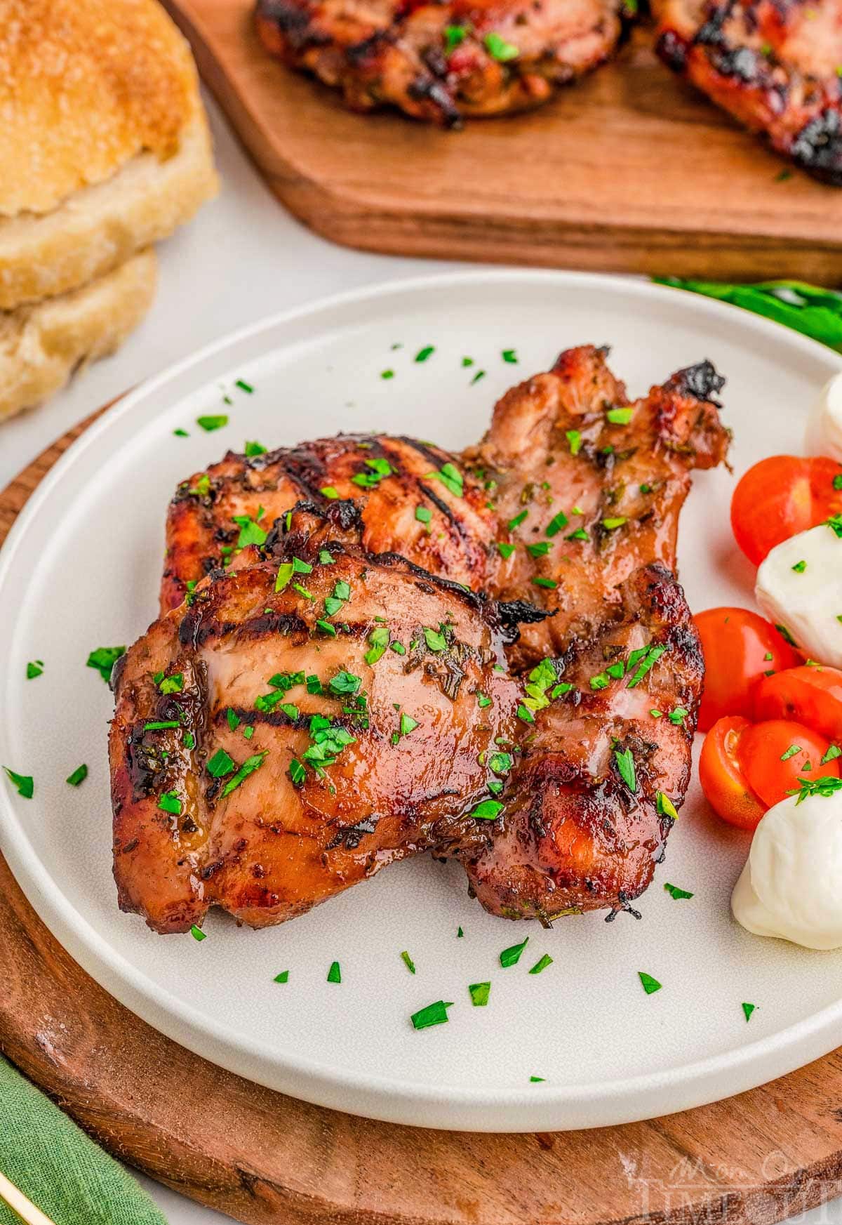 Two pieces of grilled balsamic chicken on round white plate with mozzarella and tomatoes.