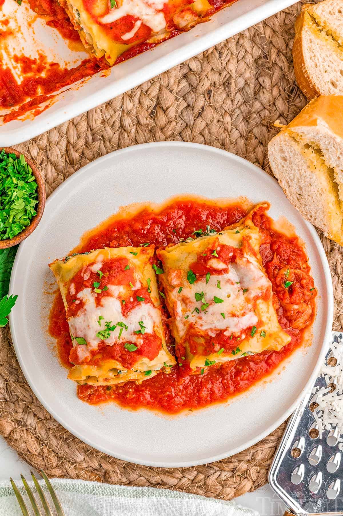 Top down look at two lasagna roll ups on a plate next to the casserole dish.