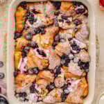 Top down look at croissant french toast bake in baking dish made with blueberries and topped with a dusting of powdered sugar.