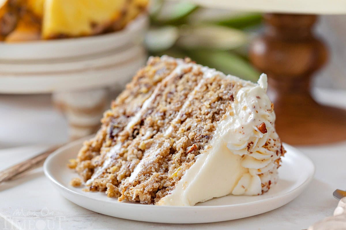 Slice of hummingbird cake on it's side on round white plate topped with cream cheese frosting.