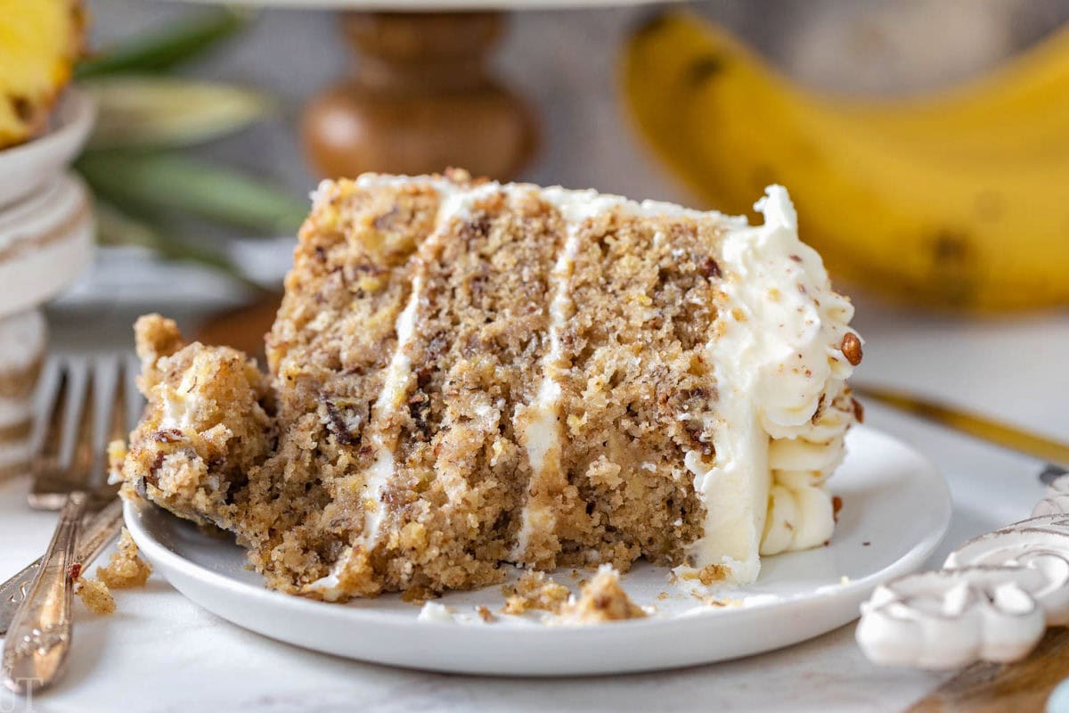 Slice of old fashioned hummingbird cake recipe on white plate with a few bites taken.