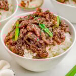 White bowl of Mongolian Beef and steamed rice topped with green onions and sesame seeds.