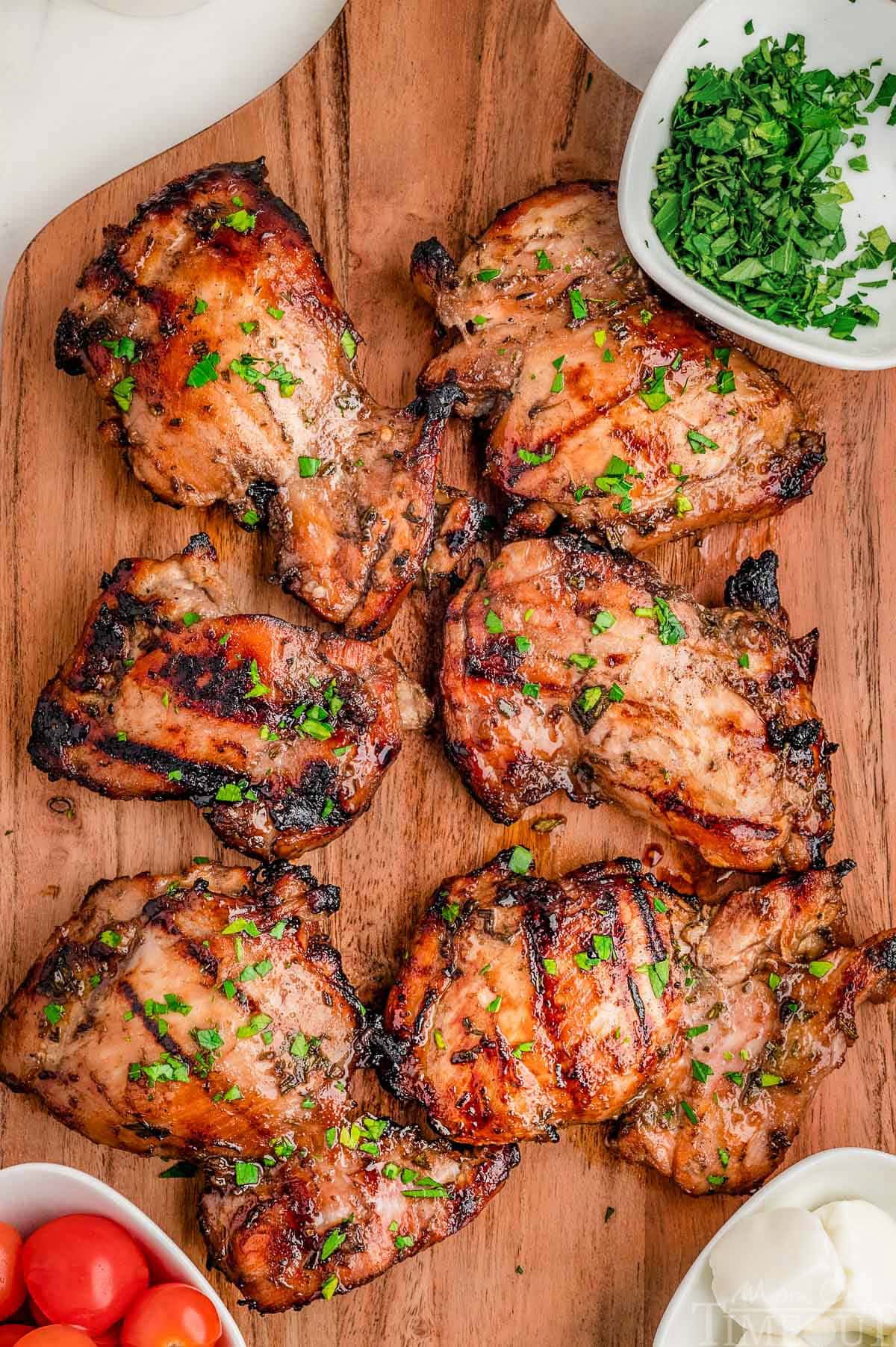 Overhead shot of six balsamic chicken thighs on wood cutting board grilled and ready to be served.