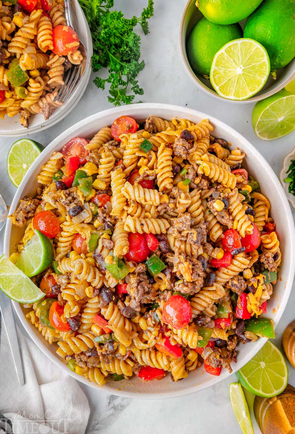Overhead shot of cowboy pasta salad recipe in large white bowl garnished with lime wedges.