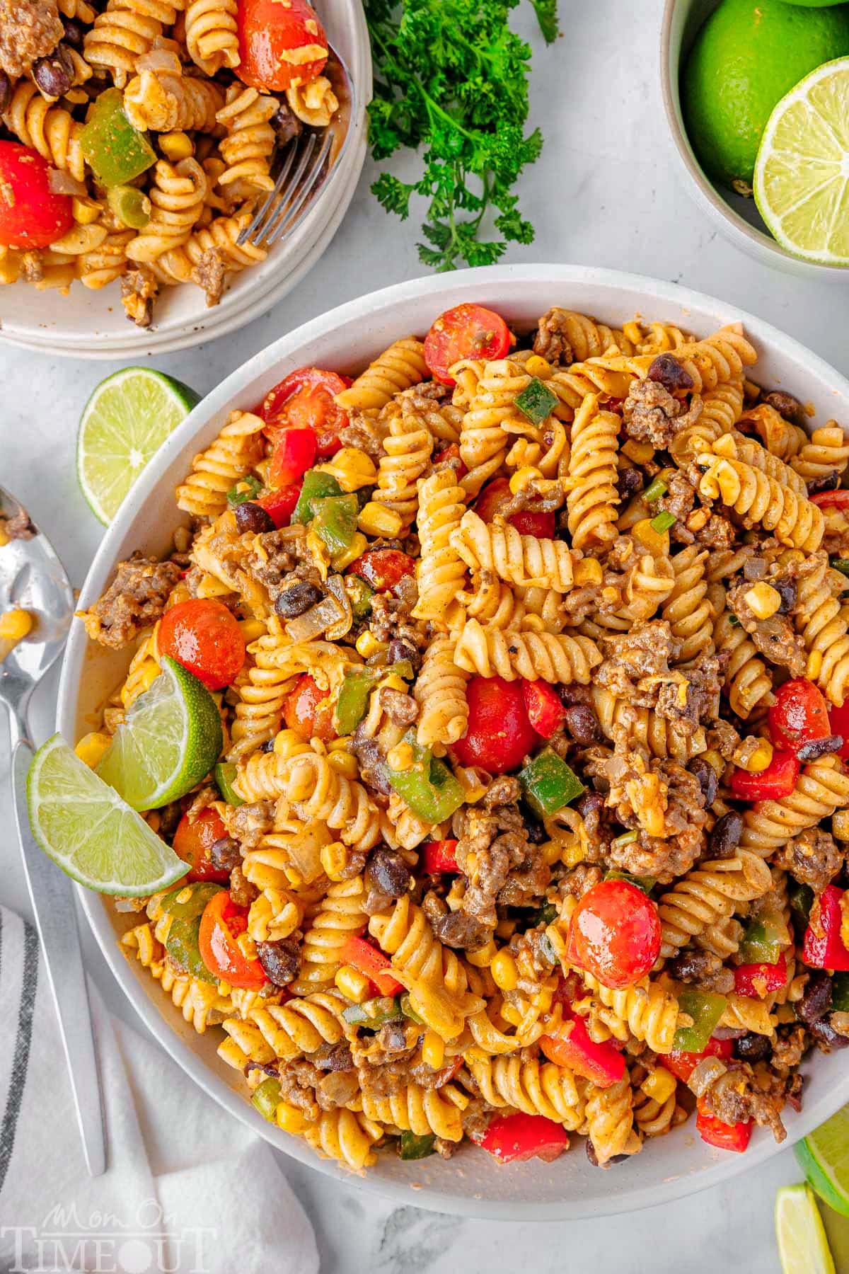 Overhead shot of two-thirds of a bowl of pasta salad made with ground beef, beans, fresh veggies and a taco-lime dressing.