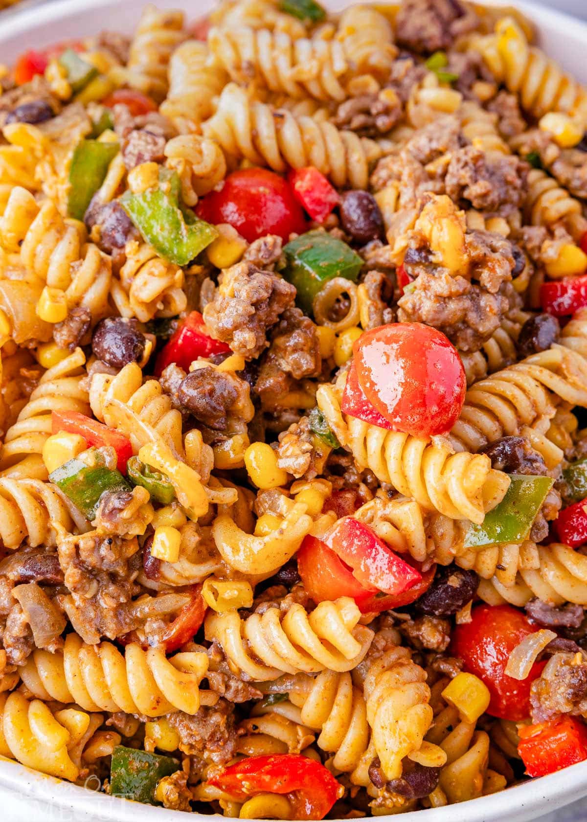 Close up look at the cowboy pasta salad recipe showing cherry tomatoes, ground beef, pasta, bell peppers, cheese and onions tossed in a zesty lime and taco dressing.