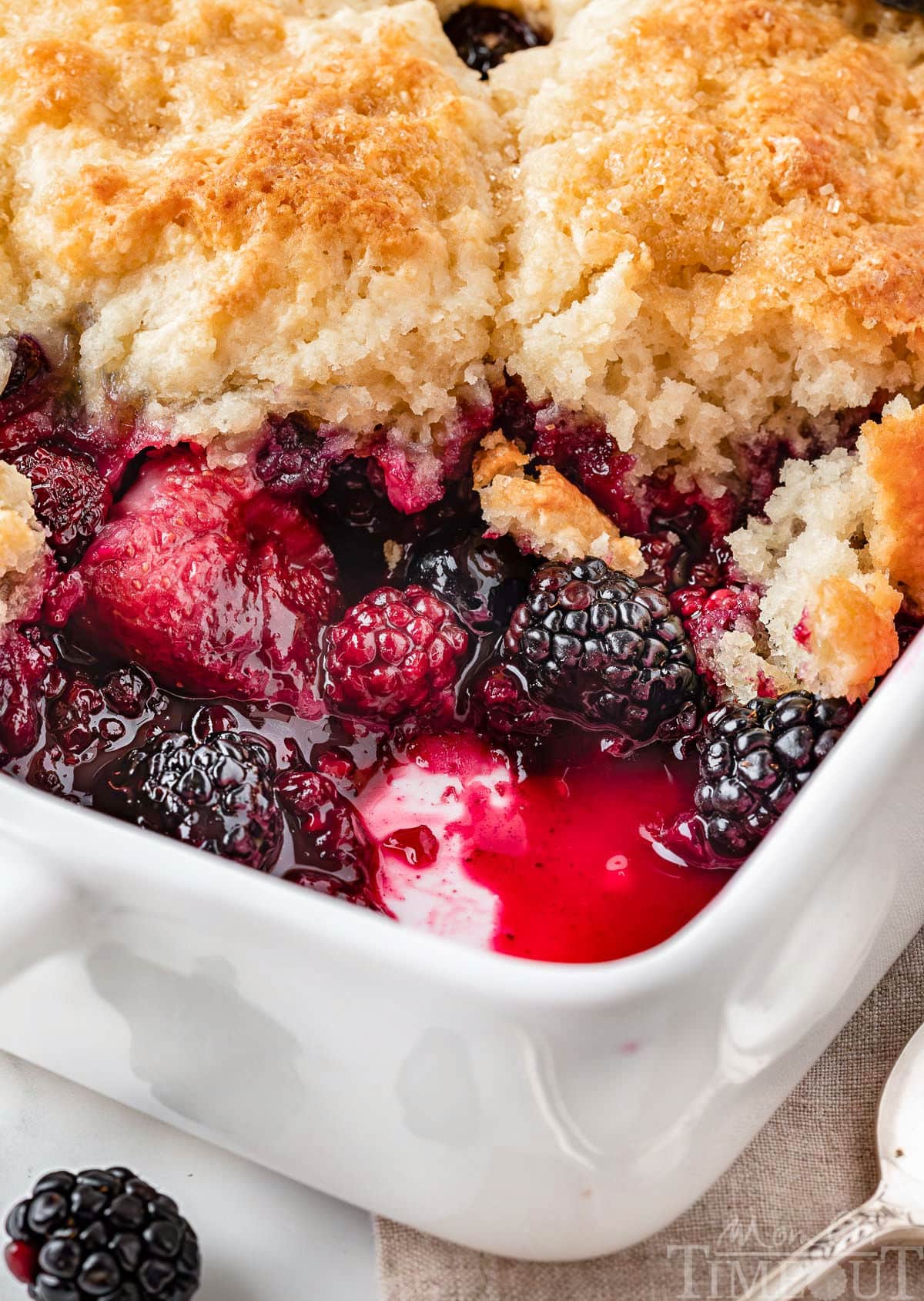 Angled view of berry cobbler recipe in white baking dish showing the mixed berries and biscuit topping.