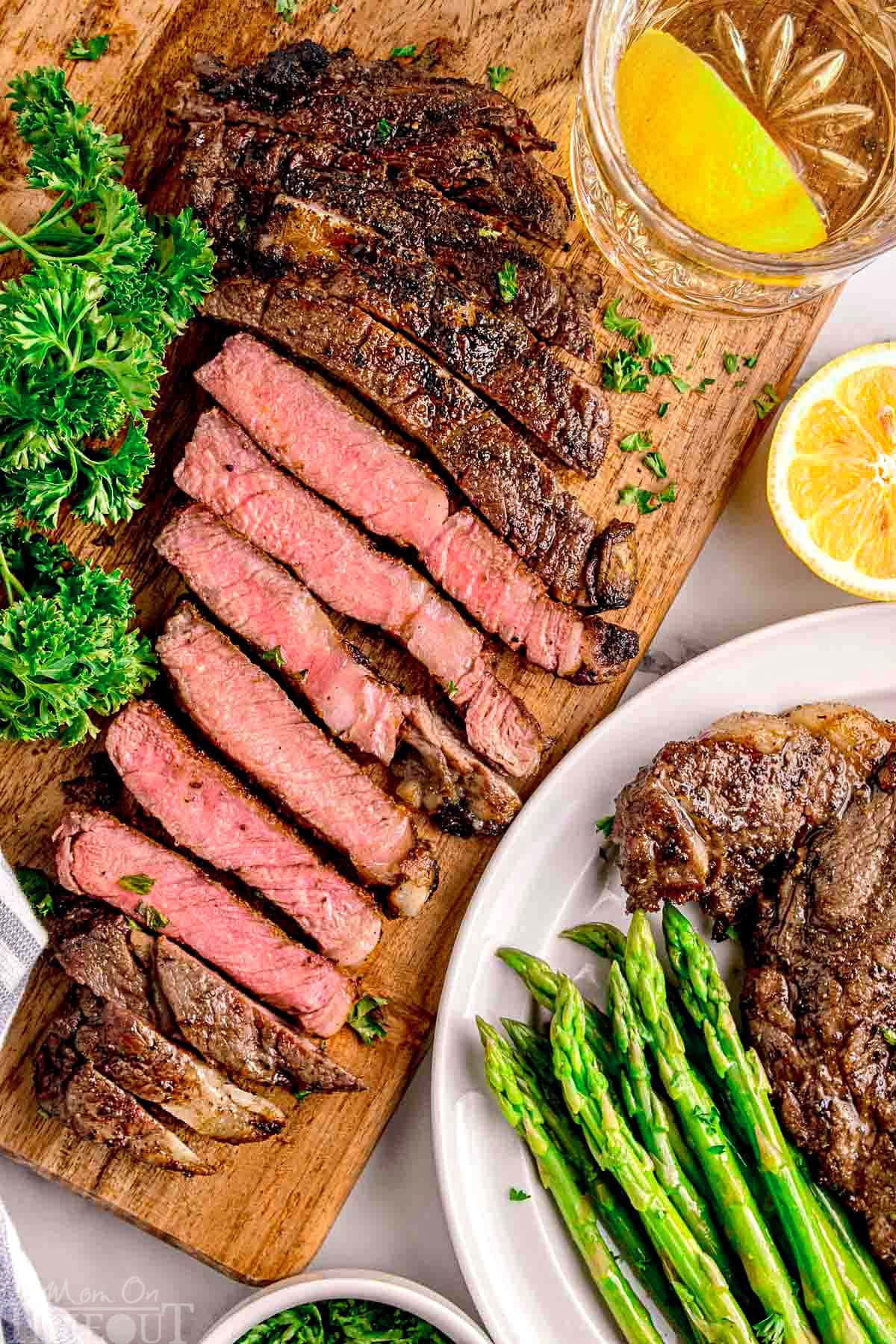 Ribeye steak cut into strips on cutting board with some plated with asparagus on a white round plate.