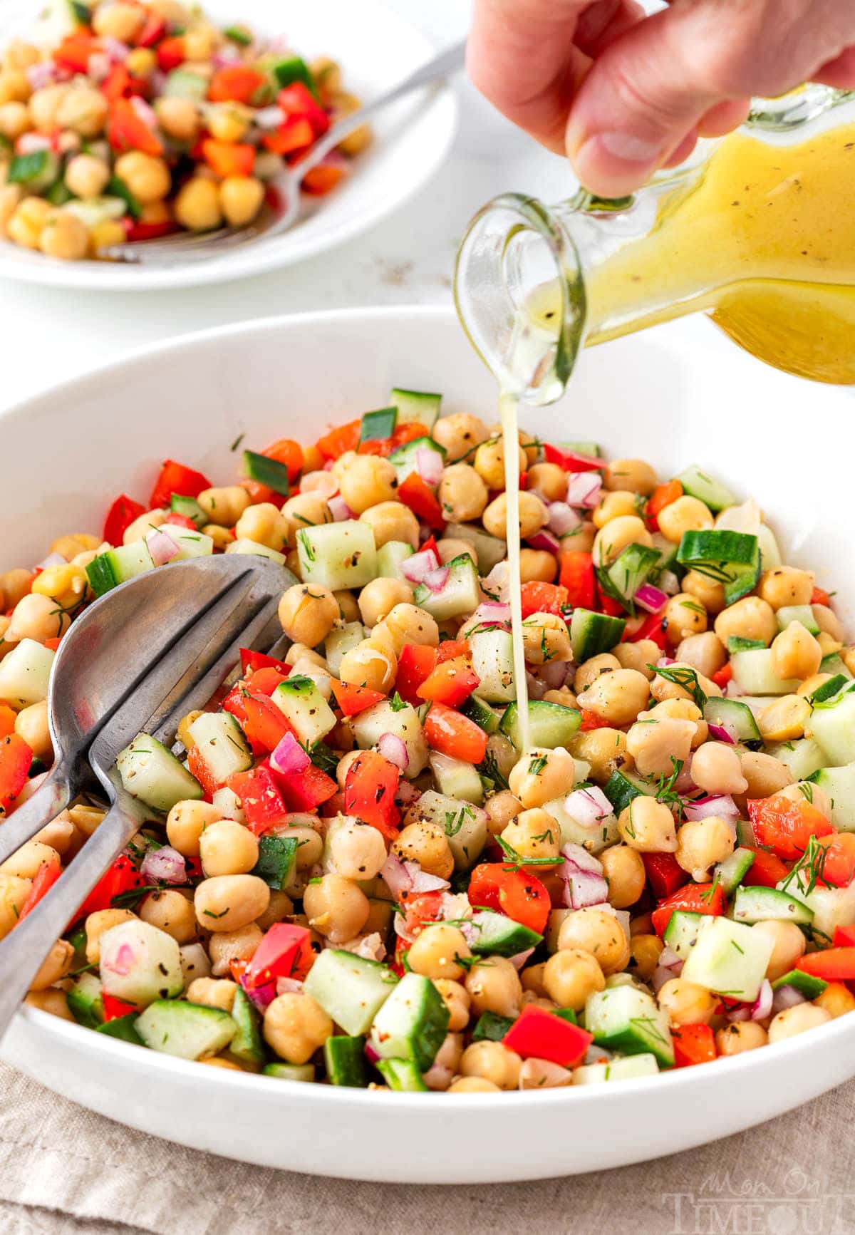 Dressing being poured over chick pea salad in a white bowl.