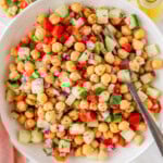 Bowl of chickpea salad recipe being held up over two small plates with the salad on them.