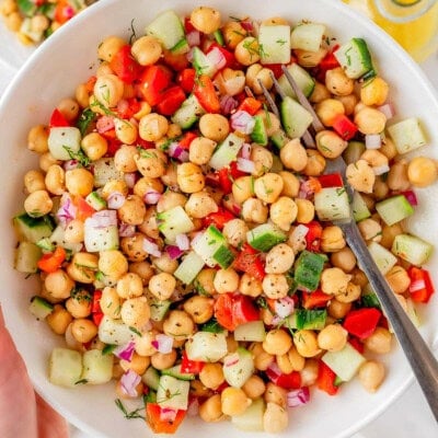 Bowl of chickpea salad recipe being held up over two small plates with the salad on them.