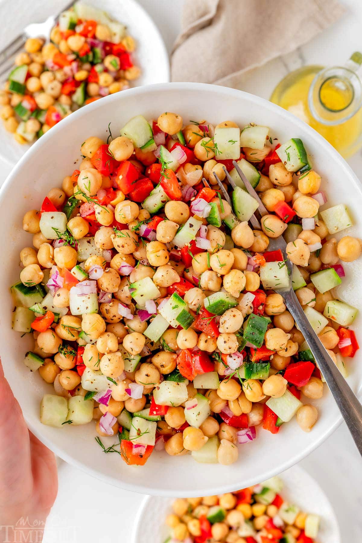 Bowl of chickpea salad recipe being held up over two small plates with the salad on them.