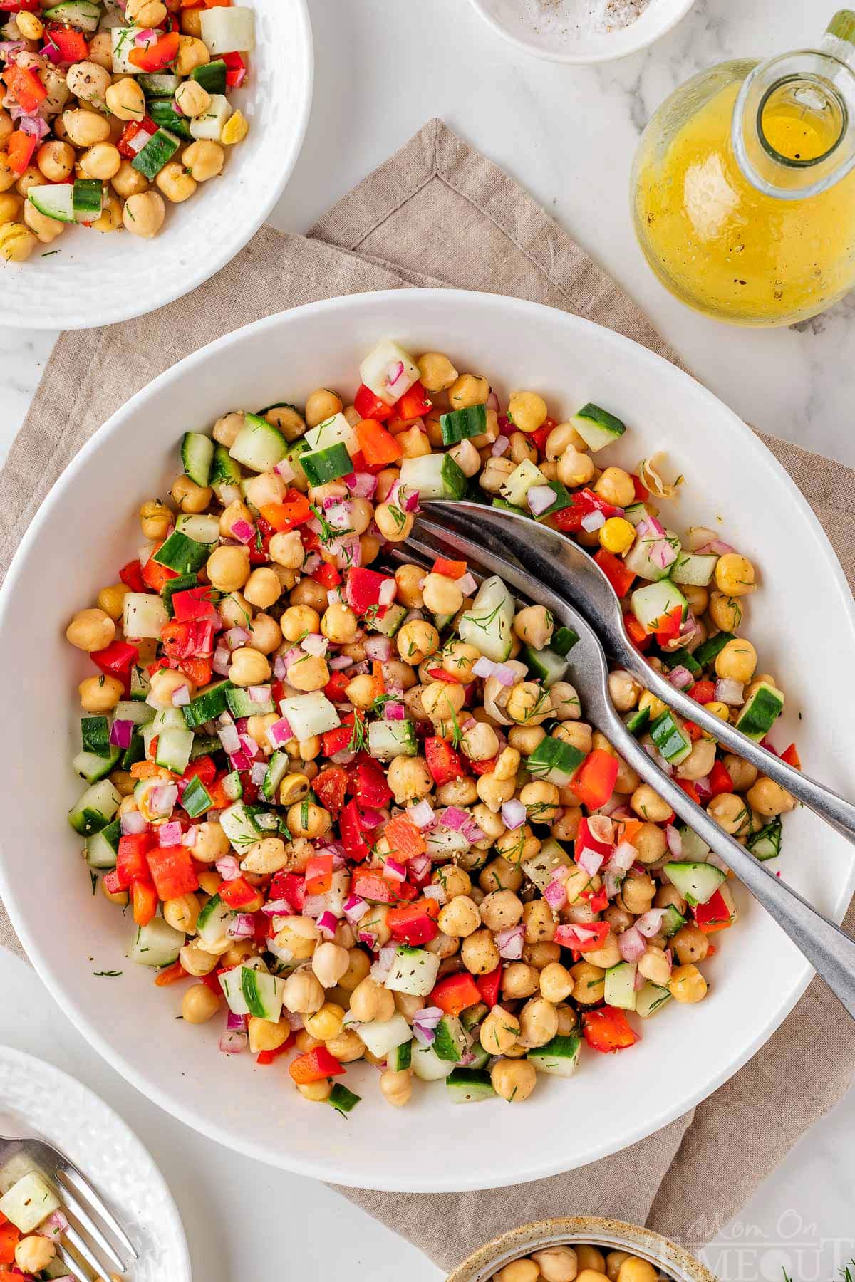 Overhead view of white bowl of chickpea salad made with cucumbers and tossed with a vinaigrette.