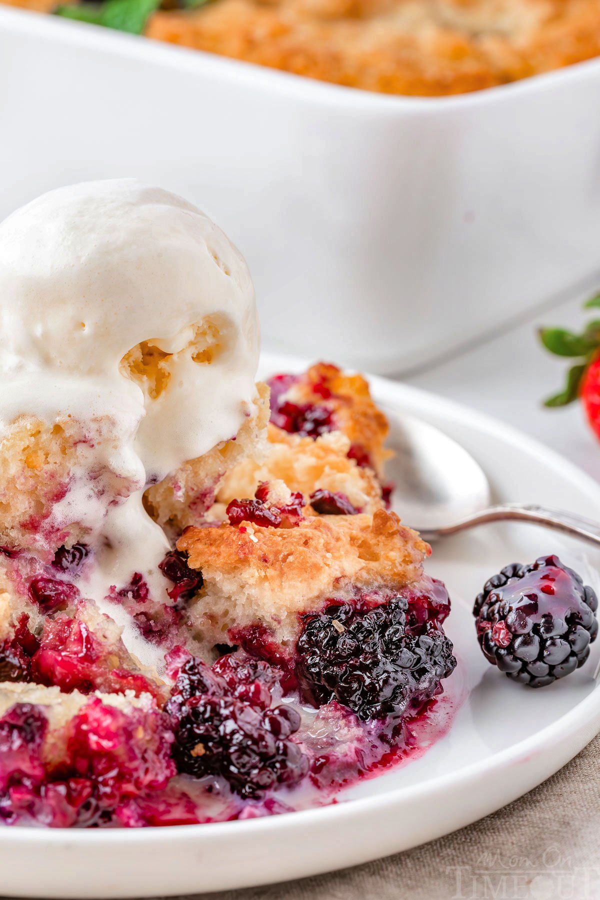Easy berry cobbler recipe on white round plate with vanilla ice cream and a spoon.