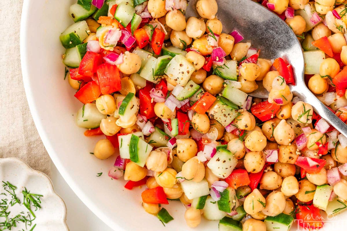 Wide shot of garbanzo bean salad in white bowl with serving spoon.