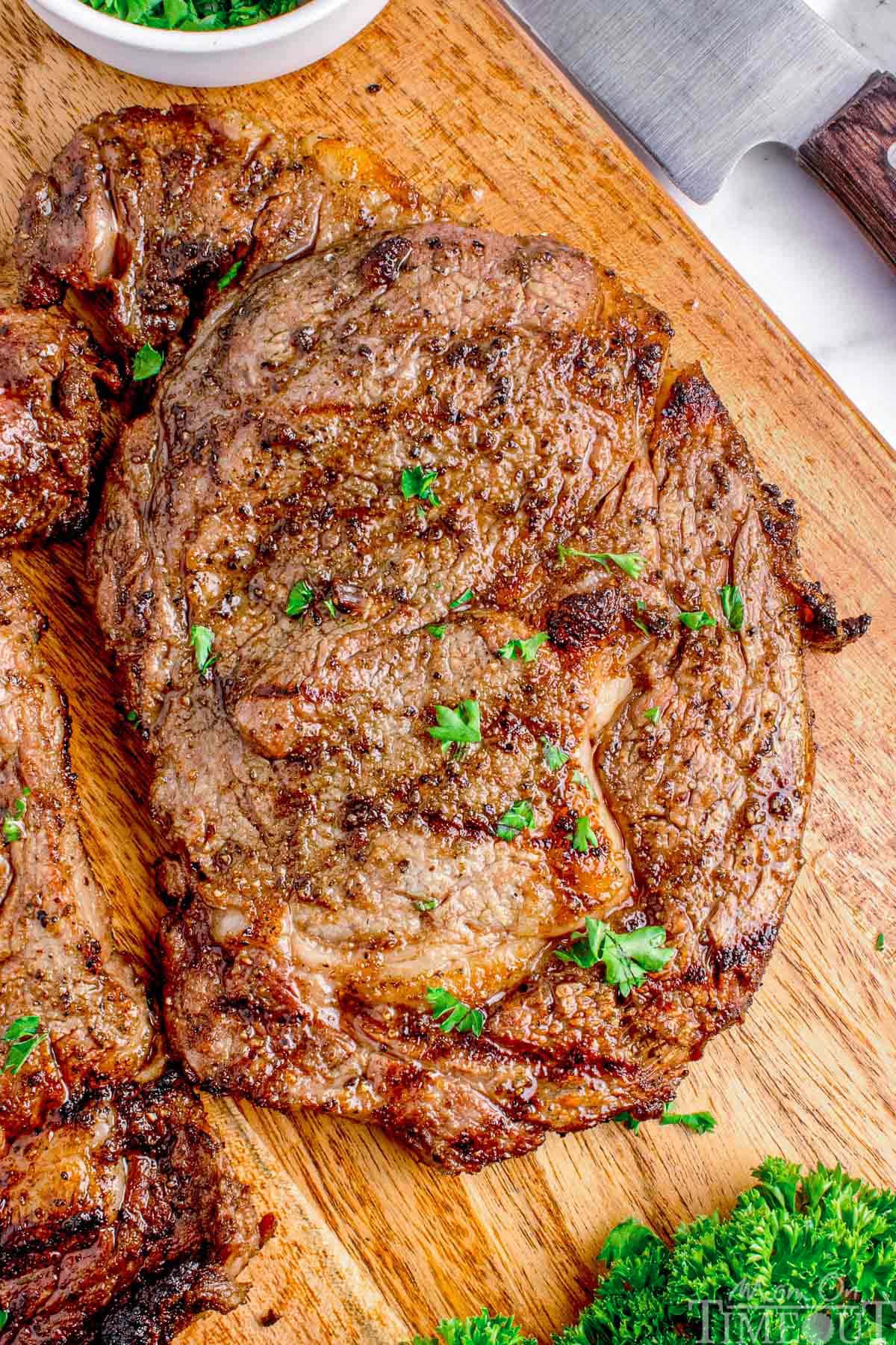 Grilled ribeye steak resting on wood cutting board.