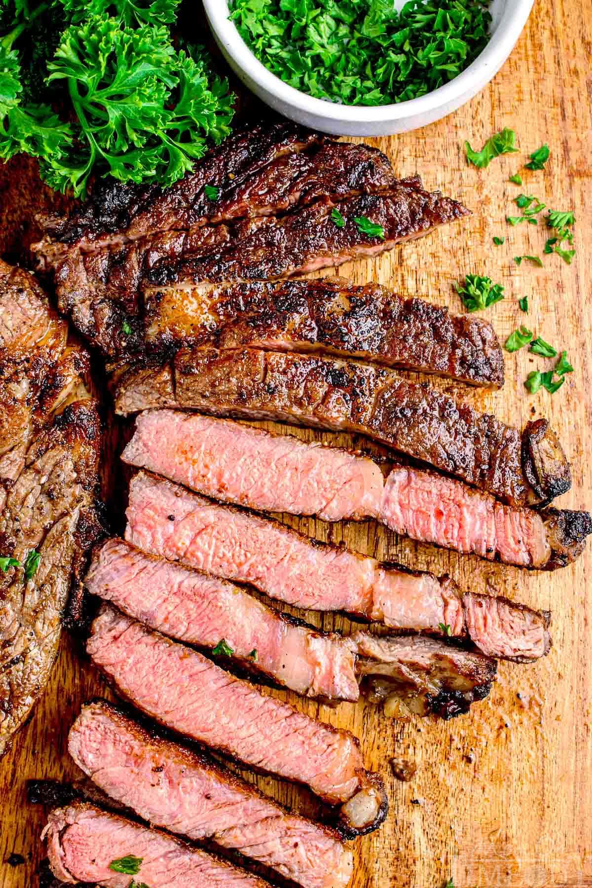 Grilled steak cut into slices showing medium doneness on a wood cutting board.