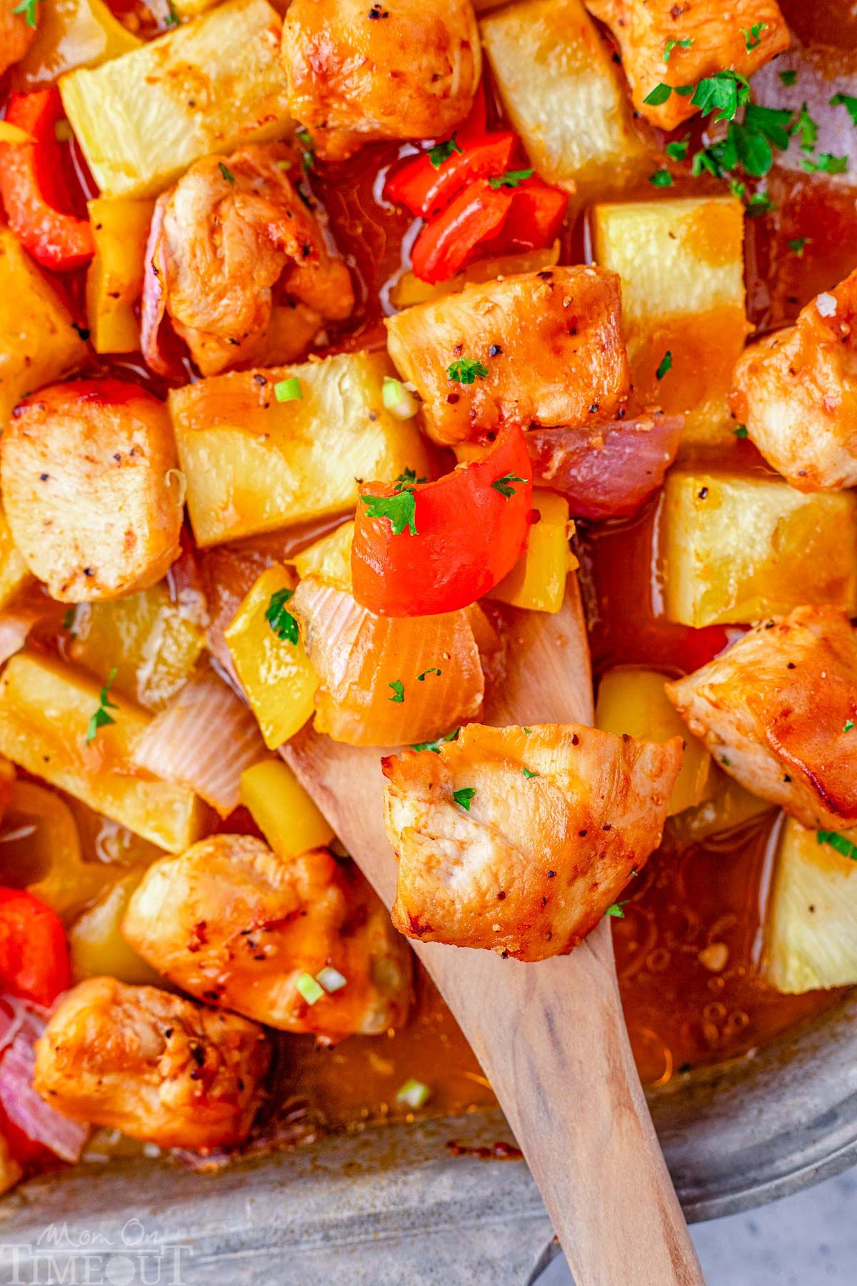 Hawaiian chicken on sheet pan with wood spoon scooping up the chicken.