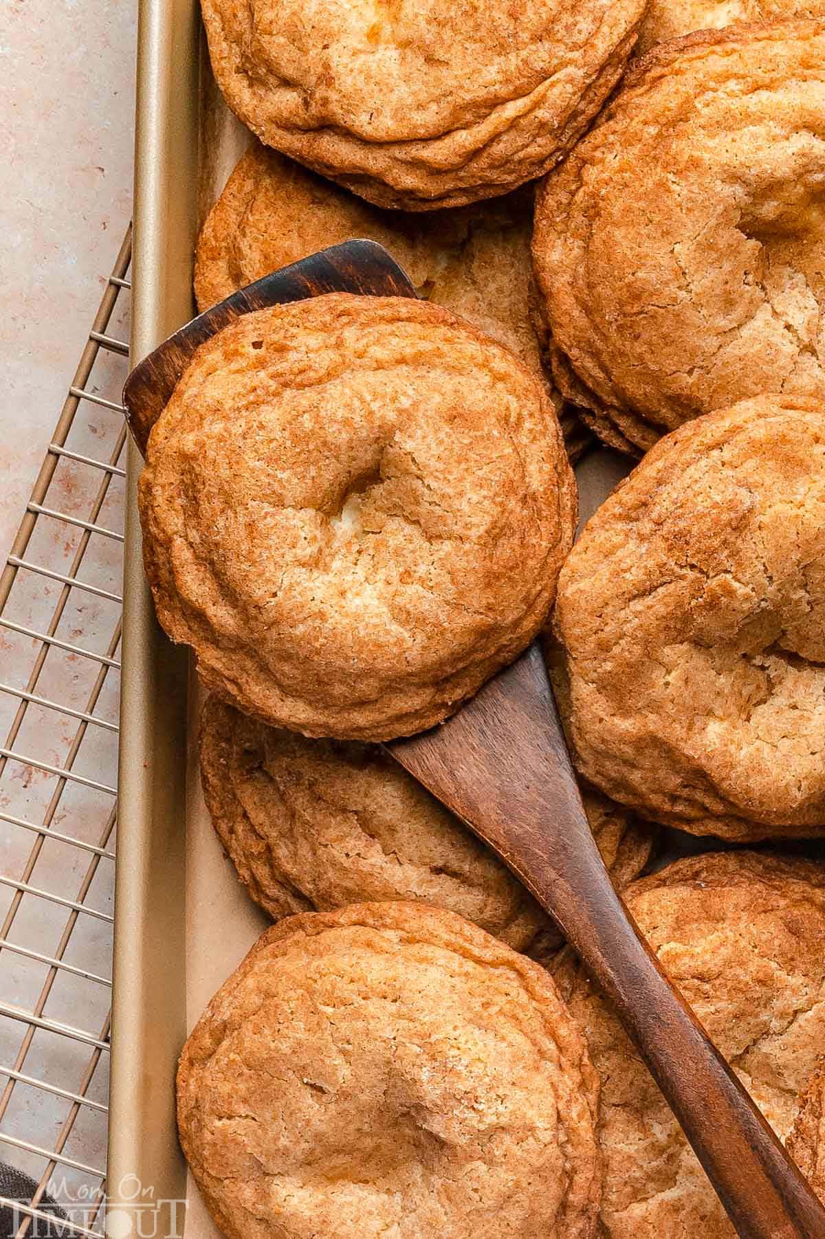 Overhead shot of cookies on sheet tray and wood spatula picking up single cookie.