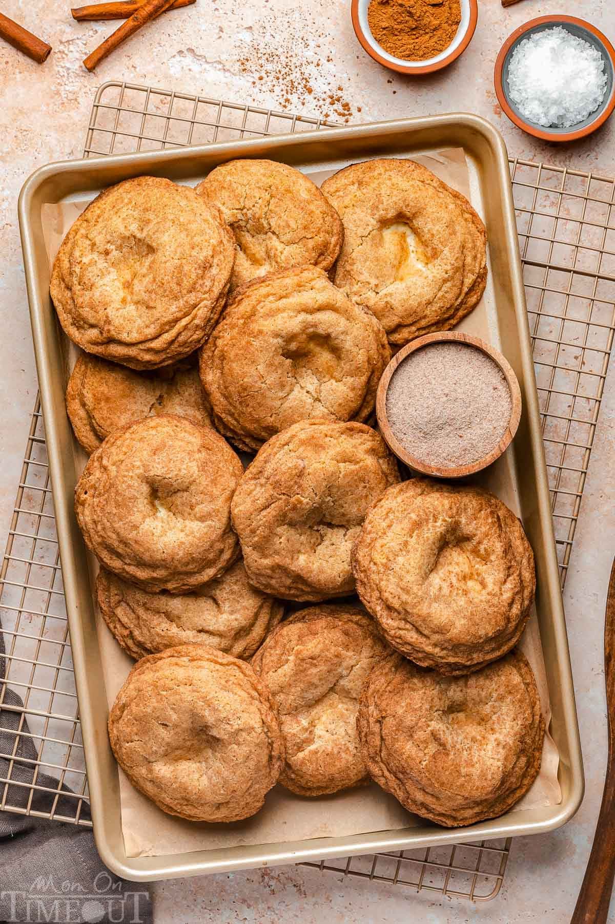 Top down shot of baked churro cheesecake cookies on baking sheet with small bowl of cinnamon sugar.